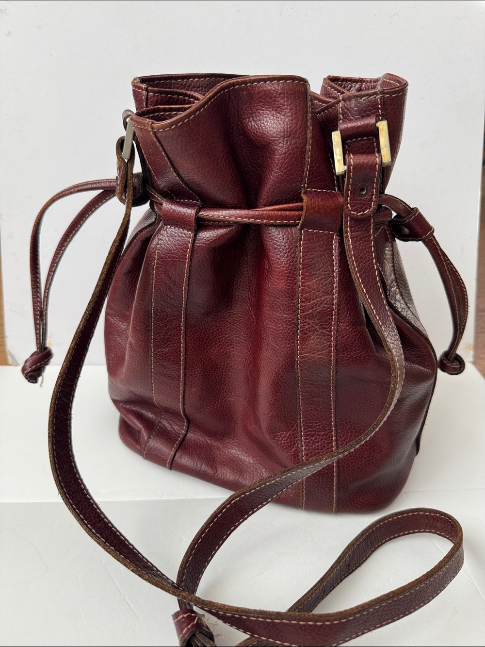 Vintage burgundy leather bucket bag with a drawstring closure and gold hardware